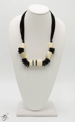 BLACK AND CREAM TOOTSIE ROLL SHAPED NECKLACE WITH BLACK PETAL DECOR ON A MULTI STRAND BLACK LEATHER-LIKE STRING